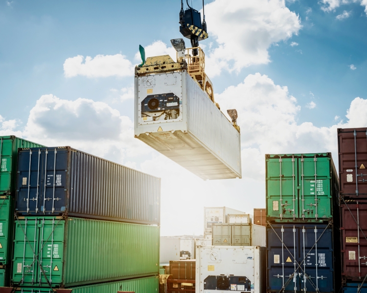 Ein Kran befördert einen Transport-Container, darunter stehen weitere Container