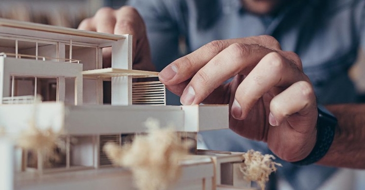 A person works on a small wood house model