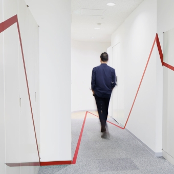 Ein Mann geht einen Gang entlang, auf den Wänden sind rote Linien zu sehen, die Wertpapierkurse darstellen sollen