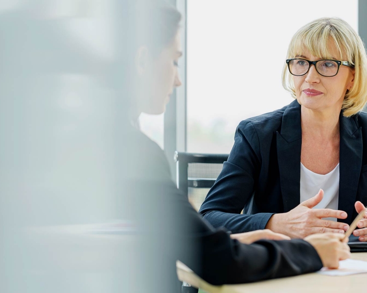 Two business women sit at a table and talk to each other
