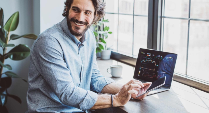 Ein Mann sitzt vor seinem Notebook und tippt auf sein Smartphone