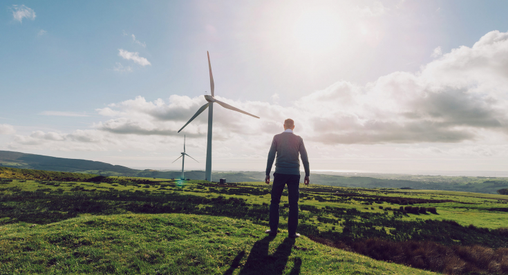 Ein Mann steht auf einem Feld und betrachtet zwei Windräder in der Ferne