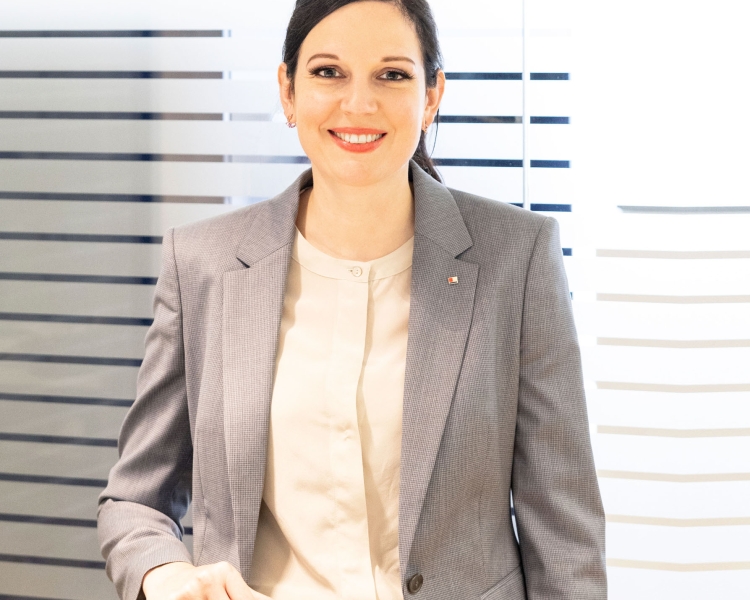 Eine Frau in einem grauen Anzug steht vor einer Glasfront