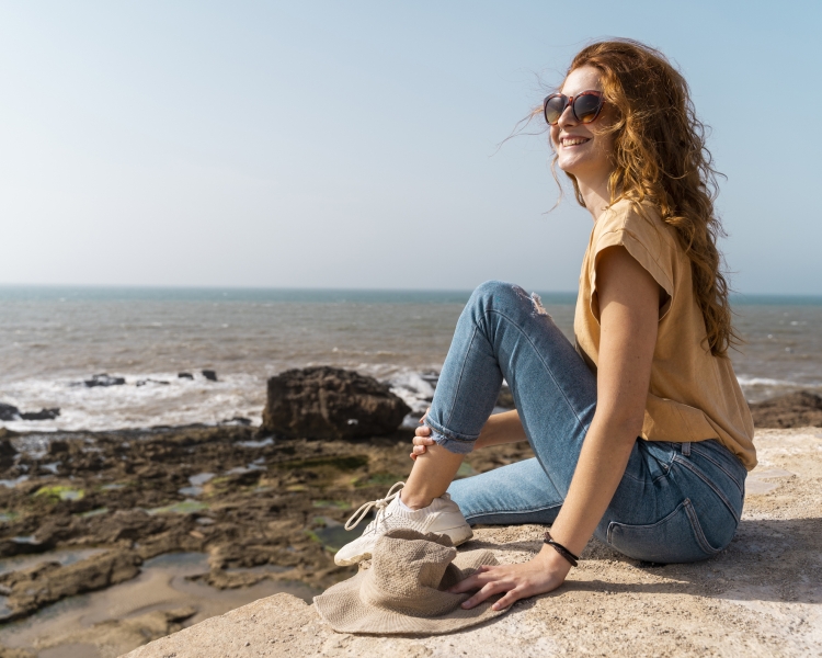 Frau sitzt in der Nähe eines Strandes und sieht in die Ferne