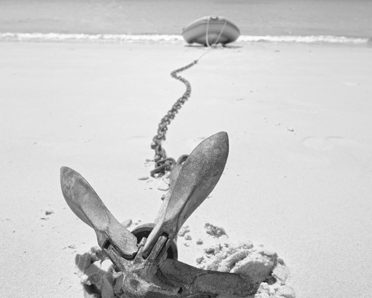 Ein Bootsanker liegt im Sand mit einem Boot im Hintergrund
