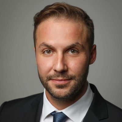 Felix Pfleiderer trägt einen dunkelblauen Anzug, ein weißes Hemd und eine blau-gemusterte Krawatte