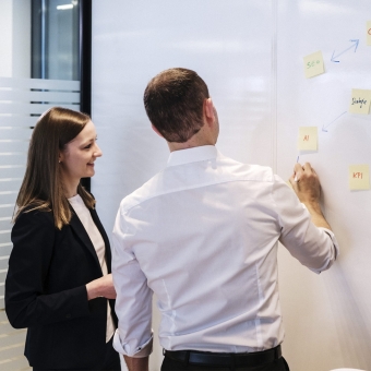 Ein Mann erklärt einer Frau etwas auf einem Whiteboard.