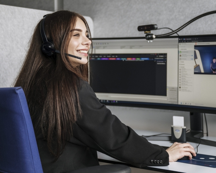 Eine Callcenter Mitarbeiterin sitzt an ihrem Schreibtisch und lächelt.