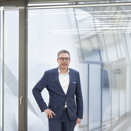 Simon Knittel, Experte für Corporate & International Finance bei der BTV Vier Länder Bank, trägt einen blauen Anzug und steht in einer Bankfiliale.