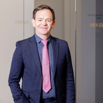 BTV Mitarbeiter Georg Lehman steht in einem blauen Anzug vor einer Glaswand in dem BTV Stadtforum in Innsbruck