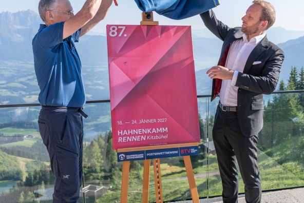 Michael Huber, Präsident des Kitzbüheler Ski Clubs, und Peter Kofler von der BTV präsentieren in Kitzbühel das Hahnenkammposter für die Saison 2027. Auf dem Poster steht: „18.–24. Jänner 2027 – Hahnenkammrennen Kitzbühel“.