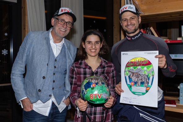 Skirennfahrer Johannes Strolz, BTV Vorstandsvorsitzender Gerhard Burtscher und Künstlerin Leonie Schalk posieren gemeinsam vor der Kamera und präsentieren den Gewinnerhelm des BTV Helmwettbewerbs.