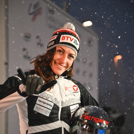Skeletonpilotin Janine Flock posiert for der Kamera im Rennanzug und hält ihren Helm in der linken Hand fest.