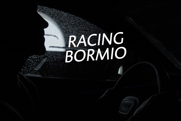Ein schwarz‑weißes Foto zeigt Skilegende Benni Raich, der im Auto sitzt. Im Vordergrund ist der Schriftzug „Racing Bormio“ zu sehen.