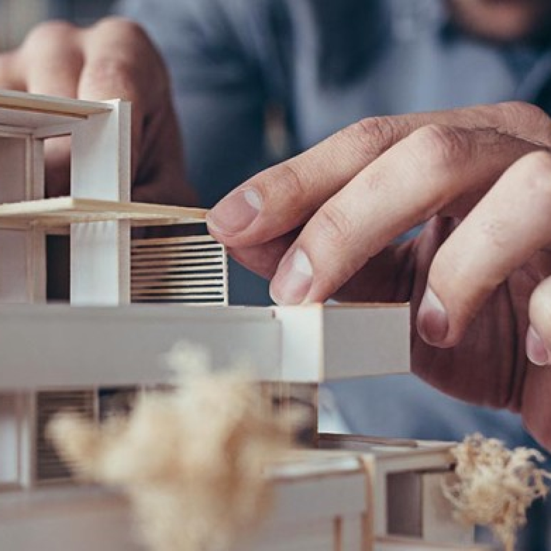 A person works on a small wood house model