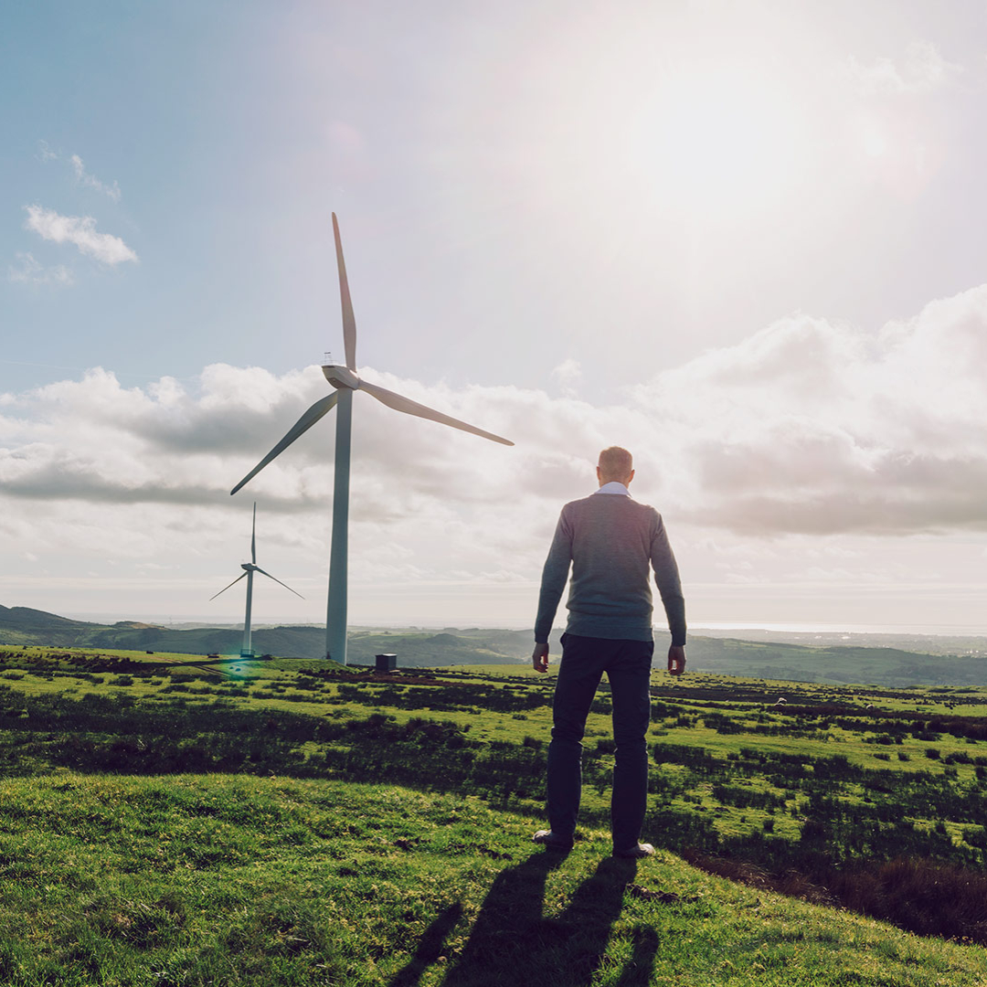 A man stands on a field and looks at two wind turbines