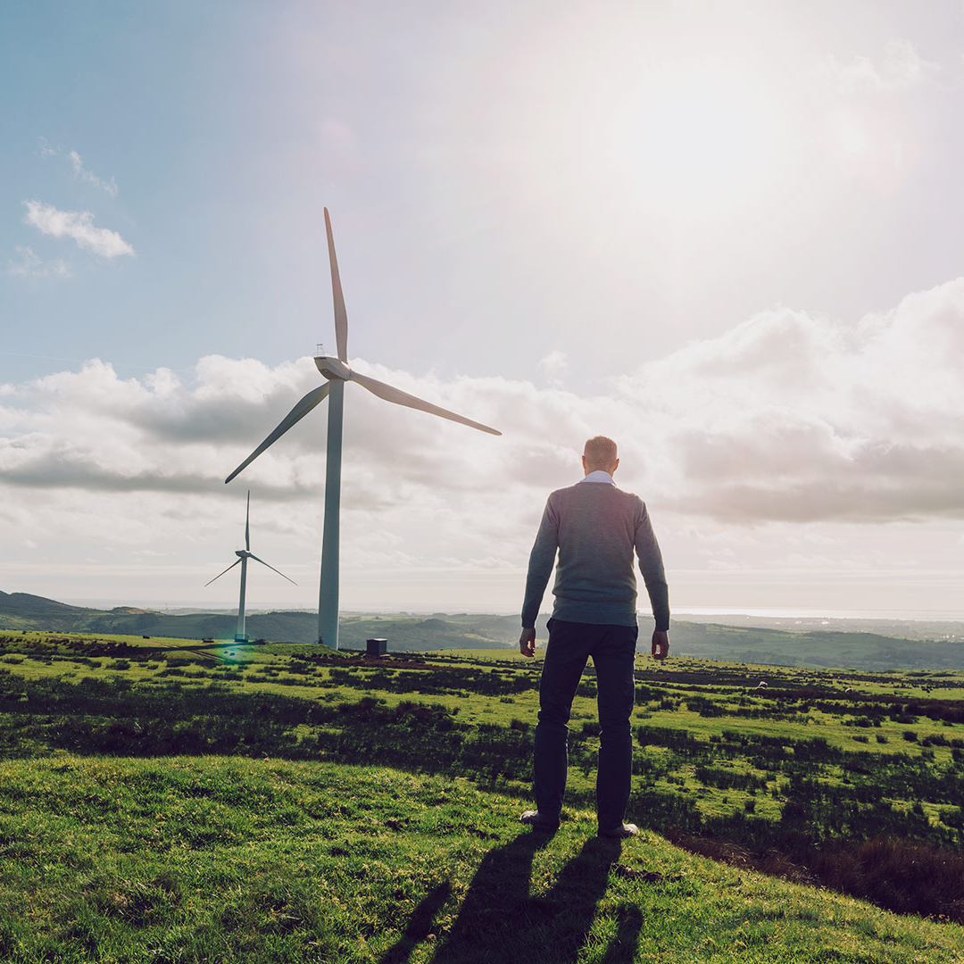 Ein Mann steht auf einem Feld und betrachtet zwei Windräder in der Ferne