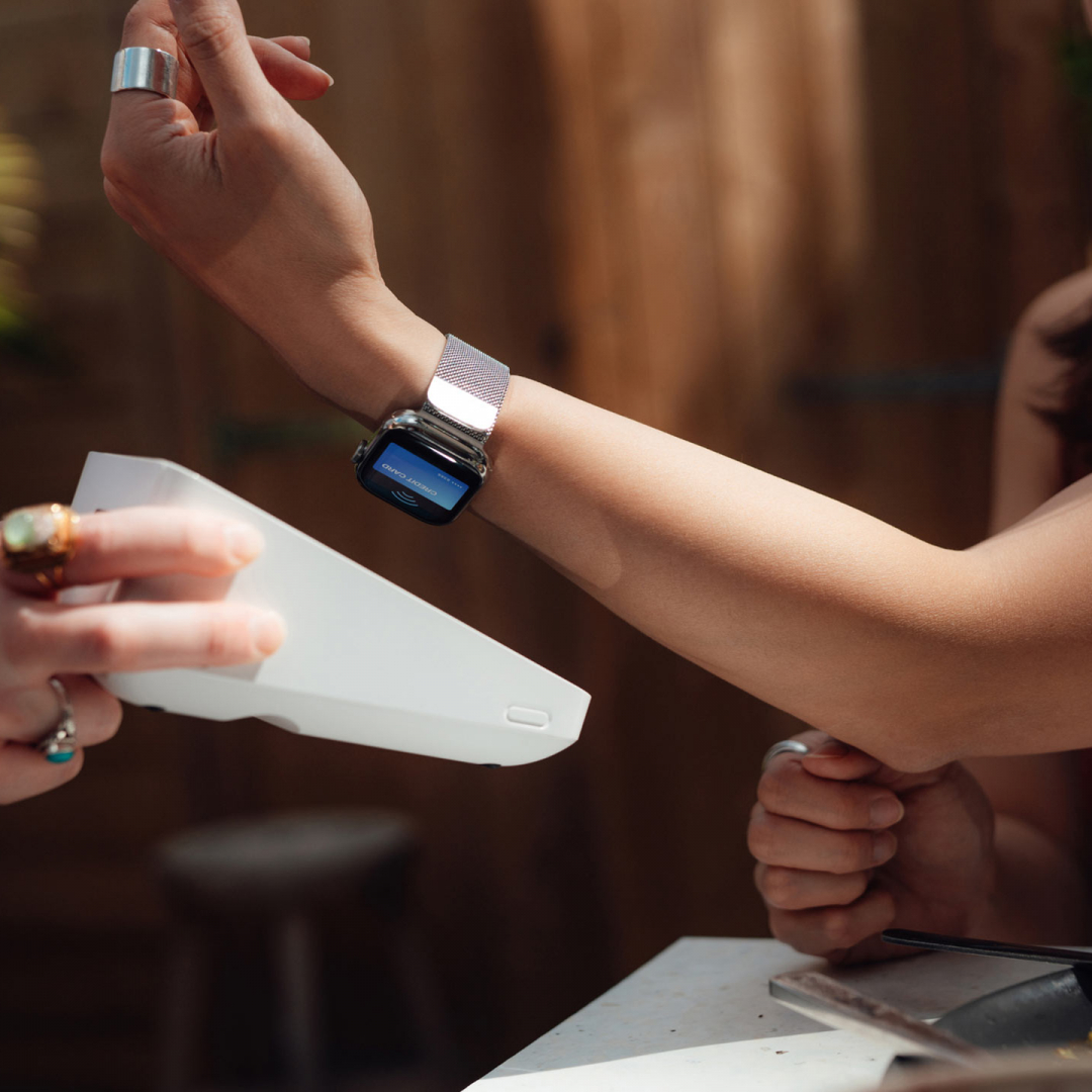 Frau bezahlt im Restaurant mittels Smartwatch bei einem tragbaren Bezahlterminal.